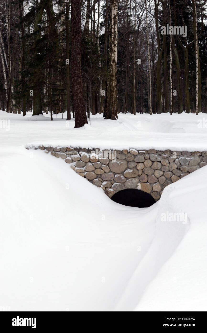 Arched stone bridge over chanel in forest covered with snow in winter time. Stock Photo