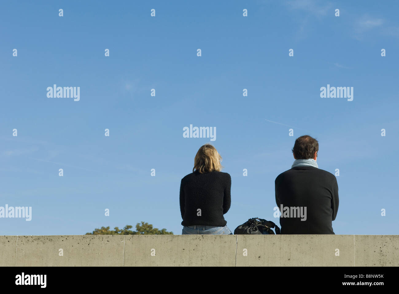 Couple sitting on ledge, rear view Stock Photo
