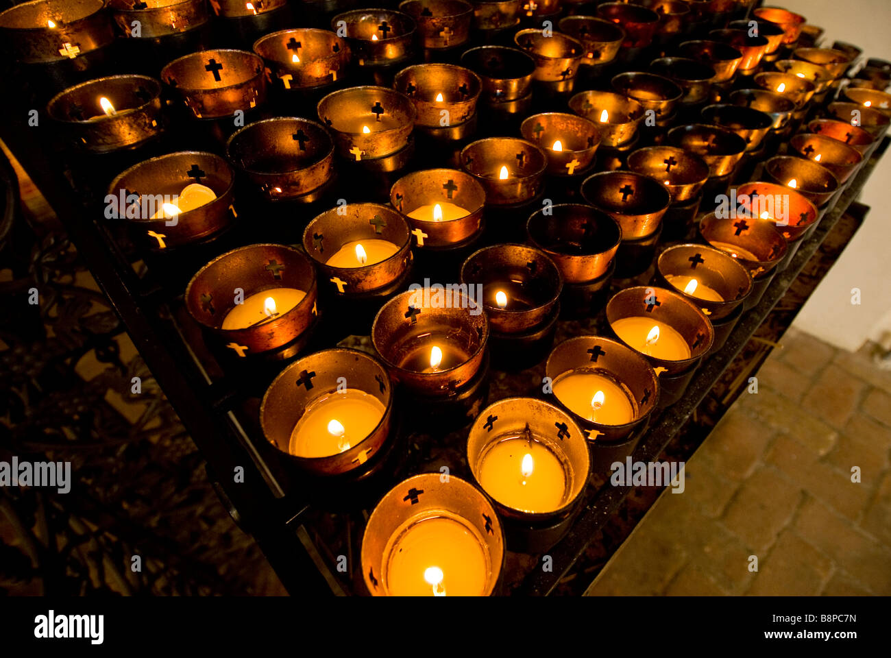 votive candles inside church rack of dozens of candles burning religious ceremony custom practice Stock Photo