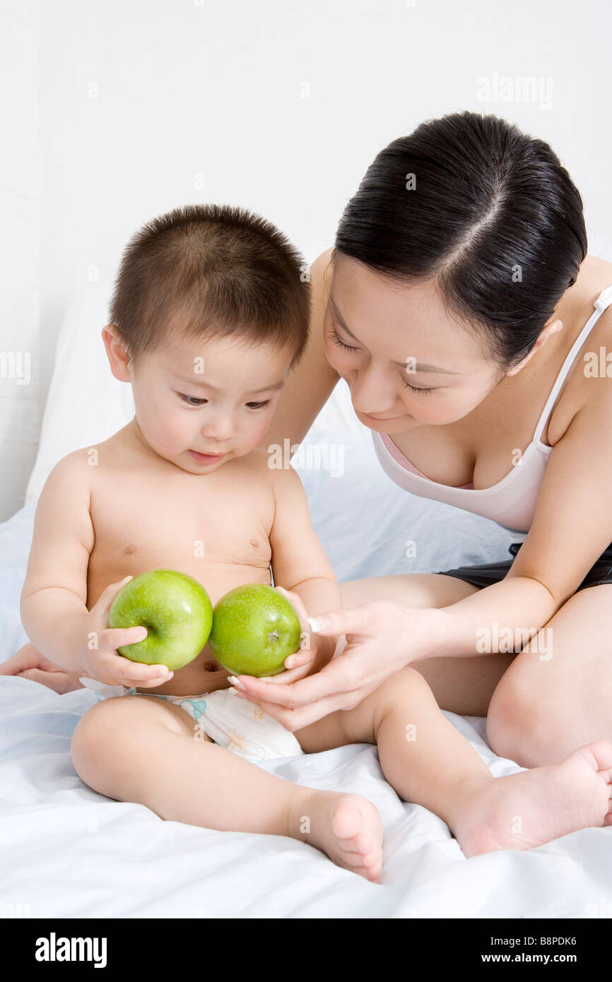 Baby boy and mother sitting on bed baby holding apples portrait Stock Photo