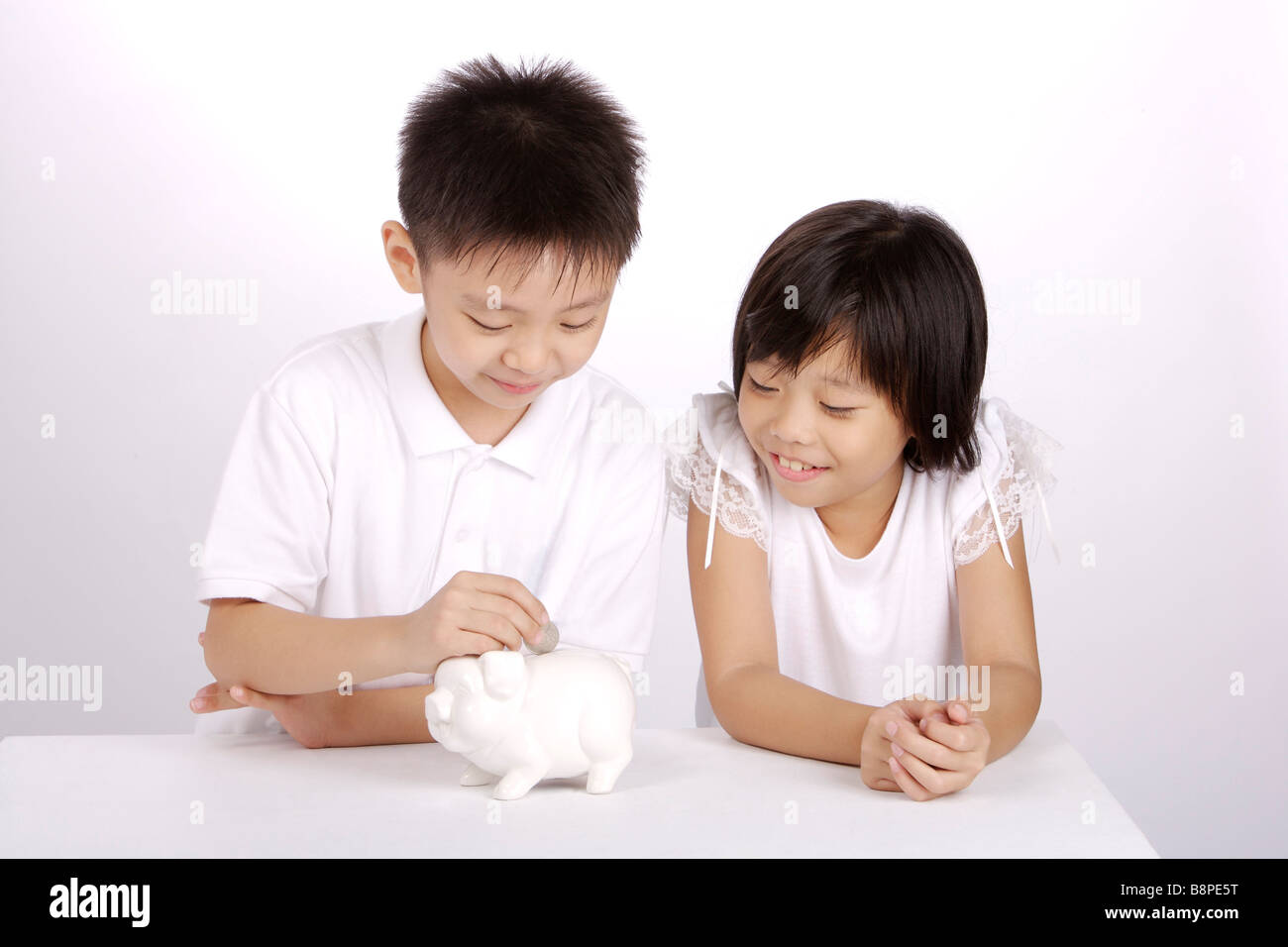 Boy putting coin into piggy bank girl looking and smiling Stock Photo ...