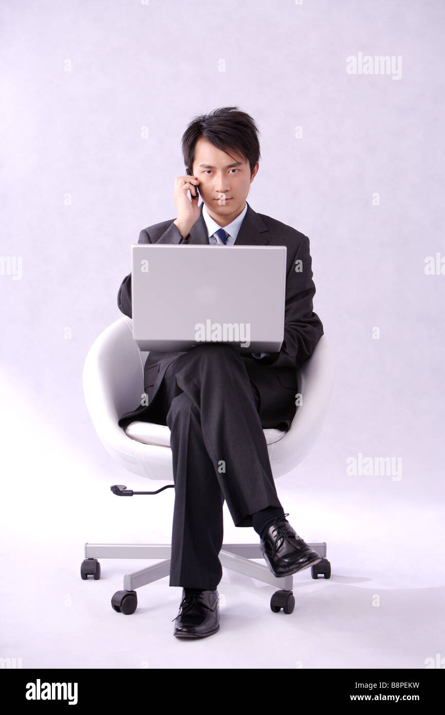Young businessman sitting with laptop on thighs looking at camera Stock