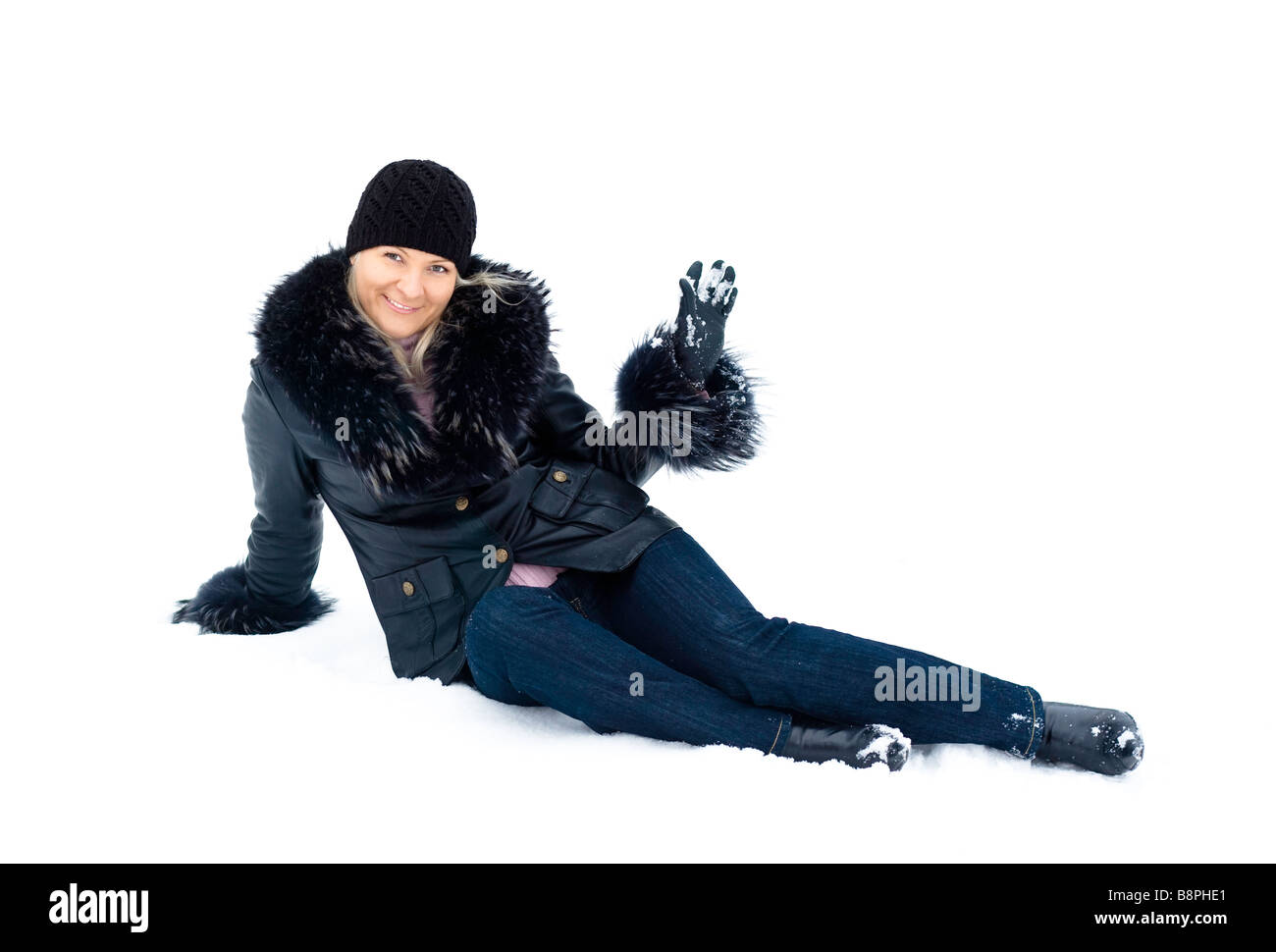 Young woman in jeans and black leather jacket with fur sitting on snow Stock Photo