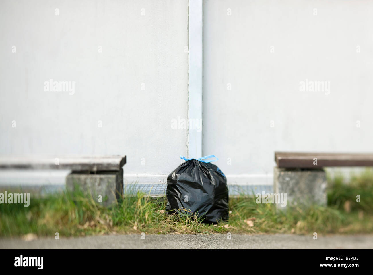 Garbage bag sitting on ground between two benches Stock Photo