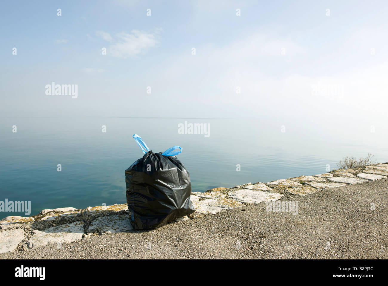 Garbage bag on ledge with sea in background Stock Photo