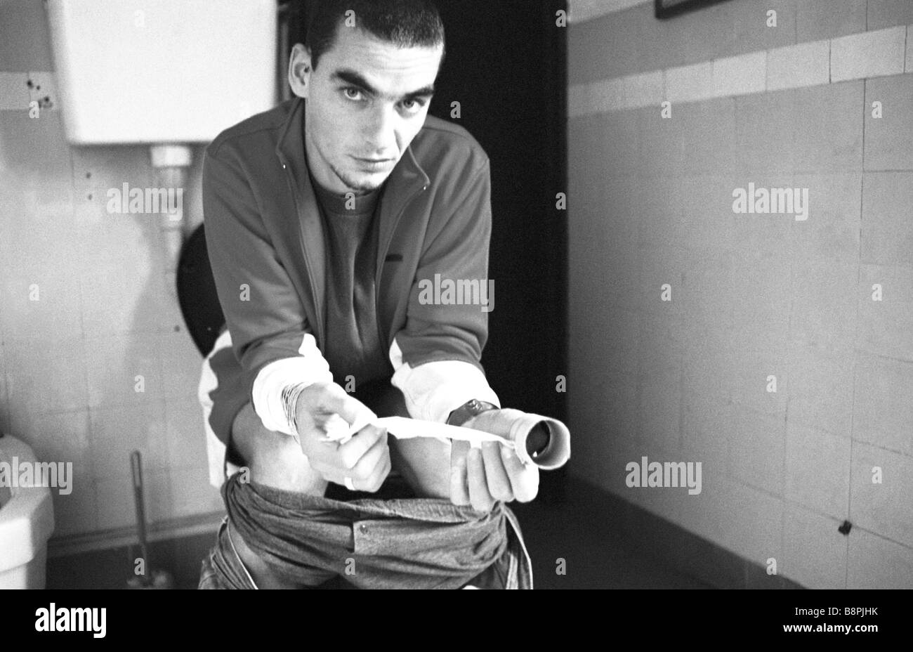 Man using toilet, holding empty roll of tissue Stock Photo