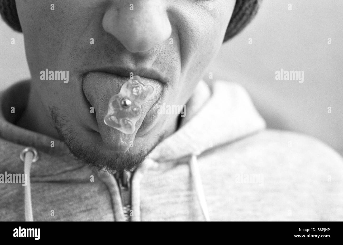 Man sticking out pierced tongue, candy bear stuck to piercing Stock Photo