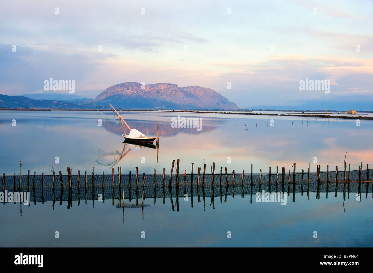 Landscape at sunrise in Mesologi- small wooden white fishing boat lays on the calm waters in the lagoon. Stock Photo