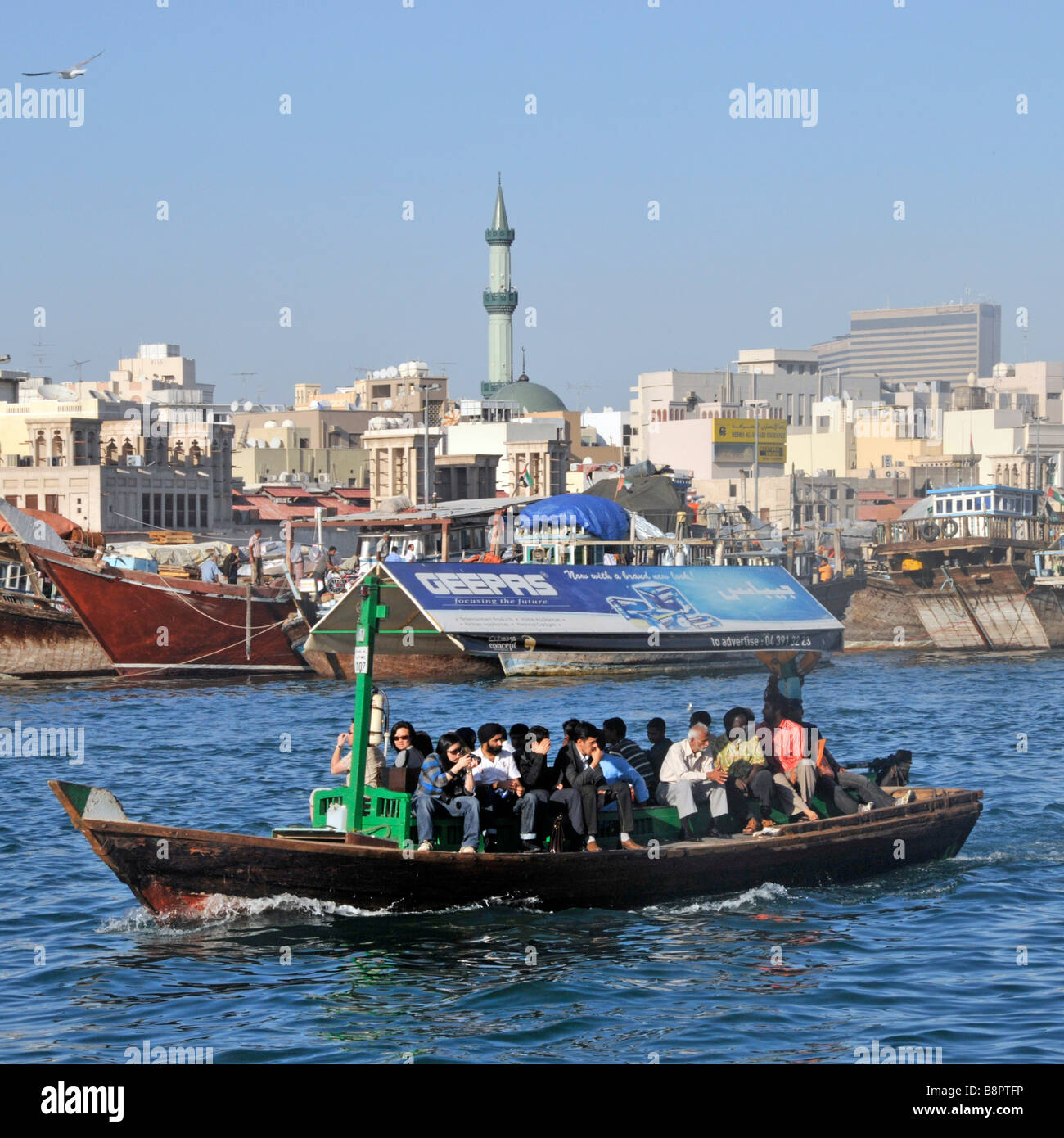 Dubai Creek close up of Abras water taxis and passengers includes older part of waterfront and mosque minaret Stock Photo