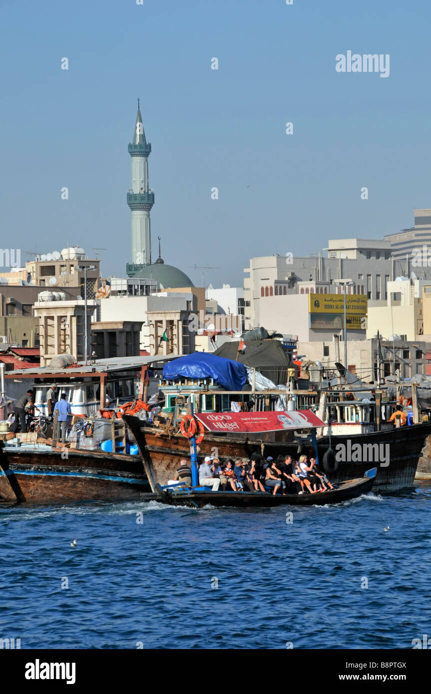 Dubai Creek close up of Abras water taxis and passengers includes older part of waterfront and mosque minaret Stock Photo