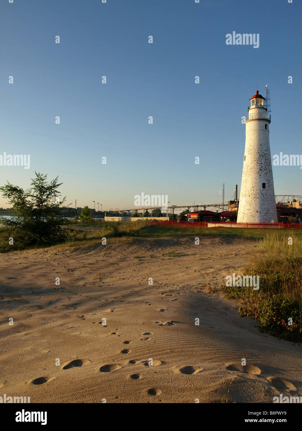 Fort Gratiot Lighthouse with Blue Water Bridge in the background and beach in foreground there are animal tracks in the sand. Stock Photo