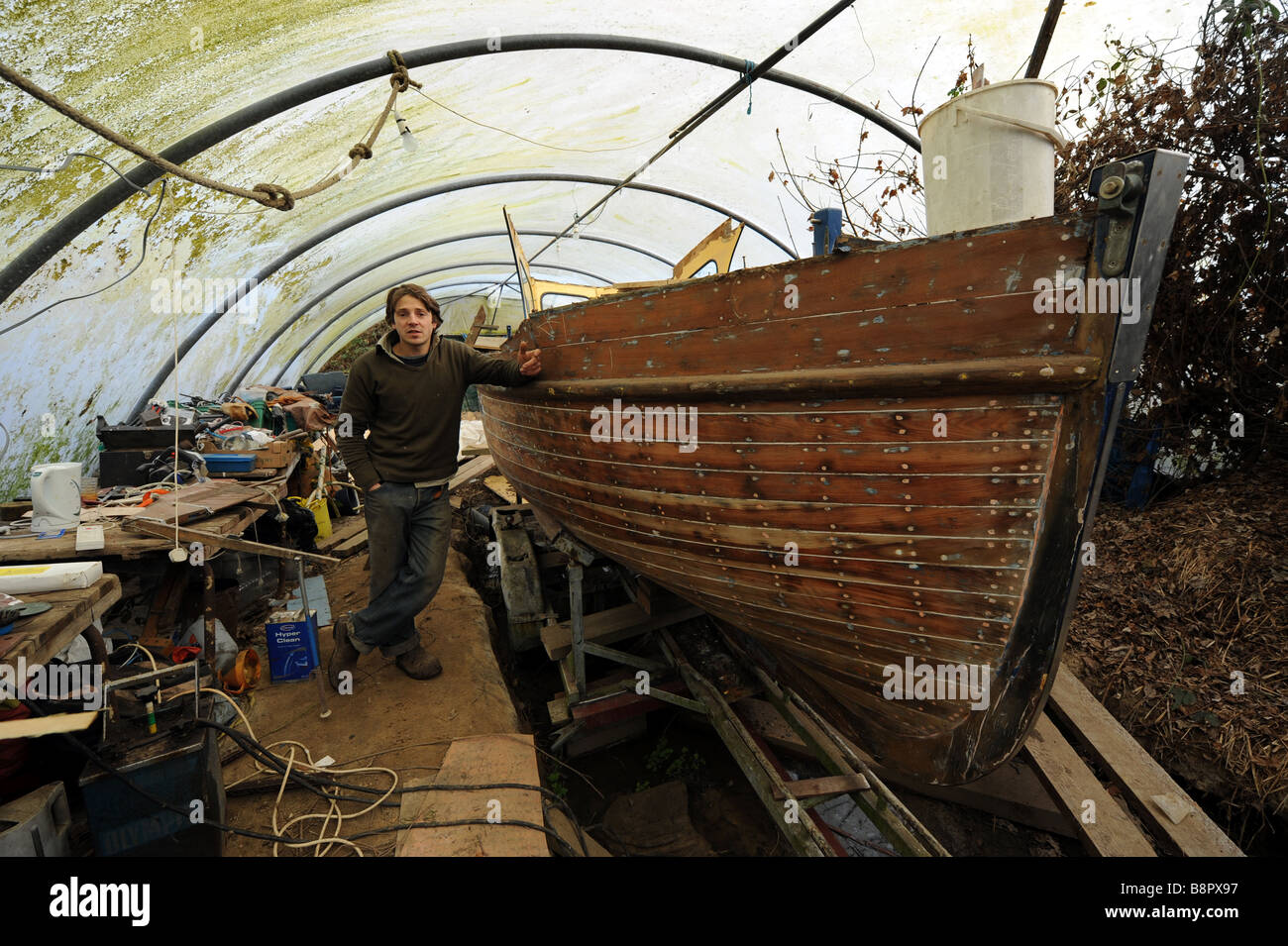 Boatbuilder and repairer Ryan Kearley amongst boats in his Barcombe workshop Sussex UK Stock Photo
