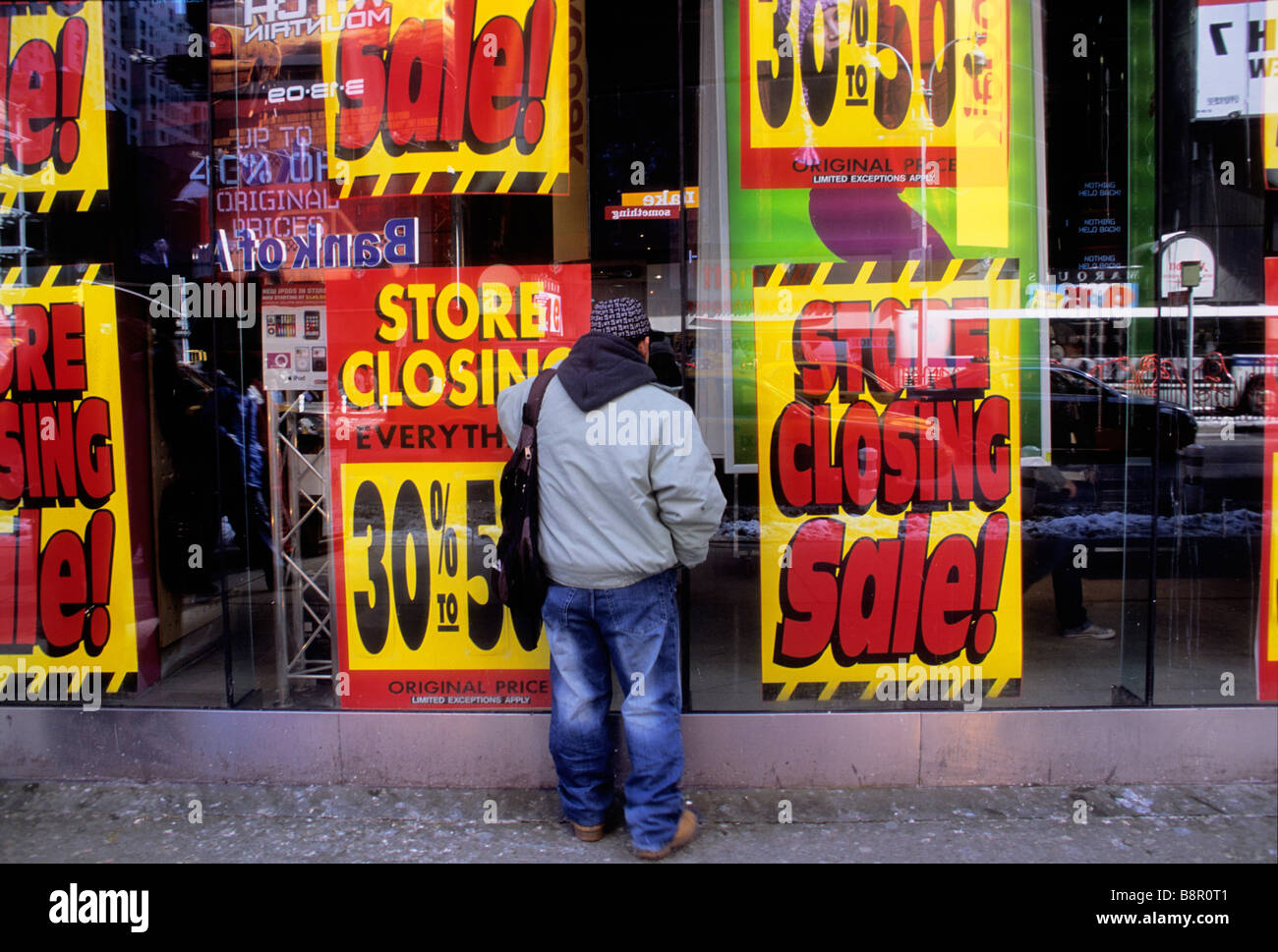 New York City store closing down sale. Man standing on the street looking at reduced liquidation prices in shop window. Store closed. Stock Photo