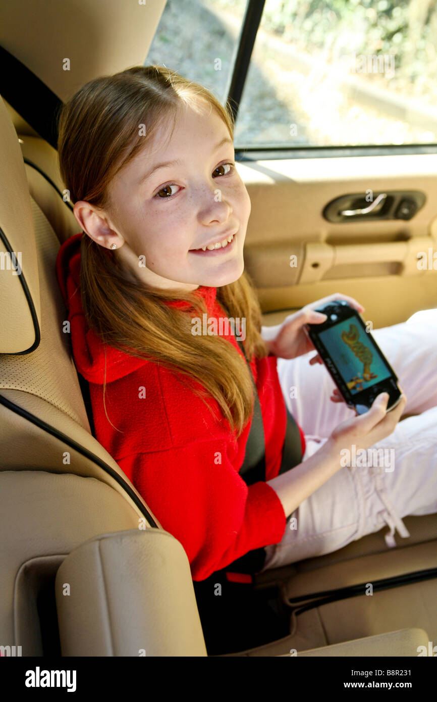 Young, happy, smiling girl  child amuses herself in the back of a car with an electronic game, psp Stock Photo