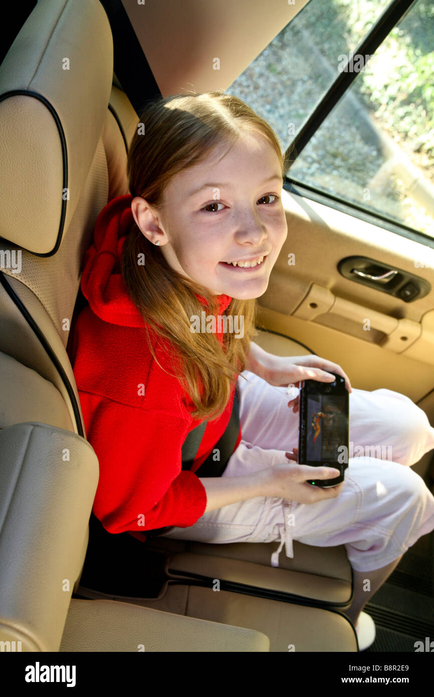 Young, happy, smiling girl amuses herself in the back of a car with an electronic game, psp Stock Photo