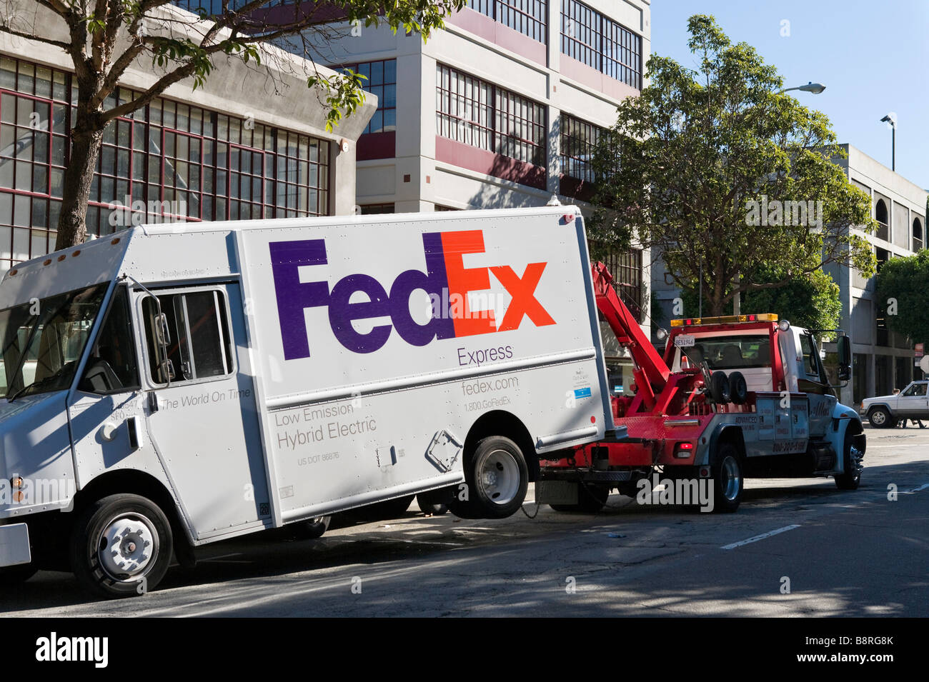 A FedEx Express hybrid electric delivery van being towed by a tow truck, downtown San Francisco, California, USA Stock Photo