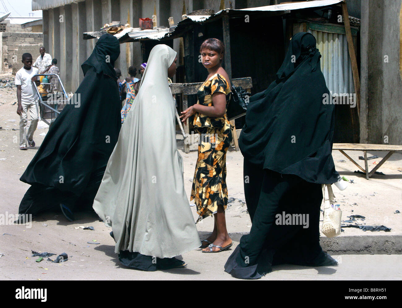 A sceptic looking modern dressed christian woman looking at muslim women wearing a full body burka. Maiduguri, Borno State, Nigeria Stock Photo