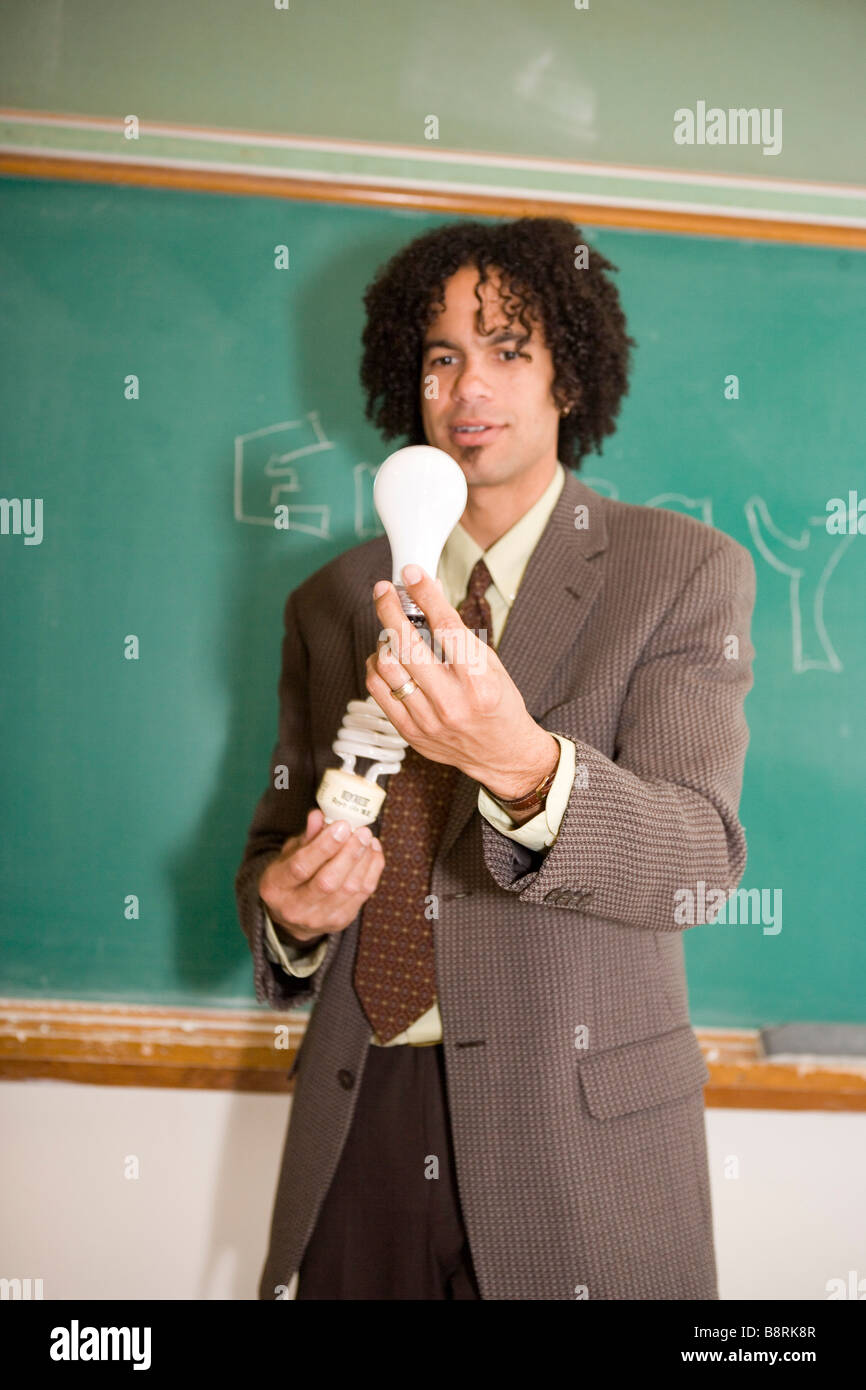 teacher in american classroom holding energy efficient compact fluorescent light bulb and traditional bulb, comparing energy use Stock Photo