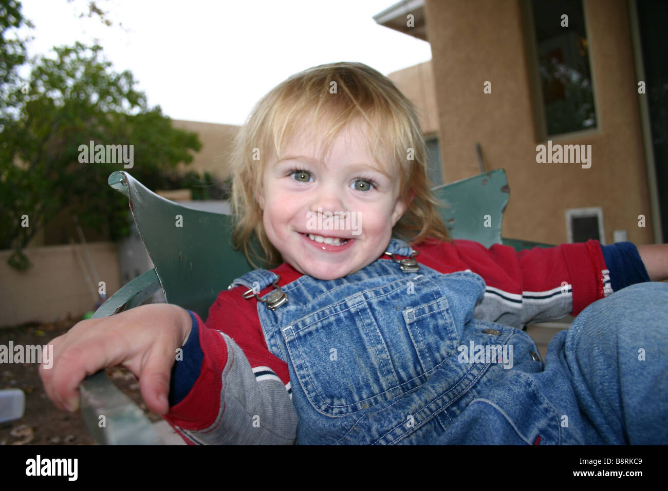 portrait of toddler sitting in a chair in backyard, smiling, wearing