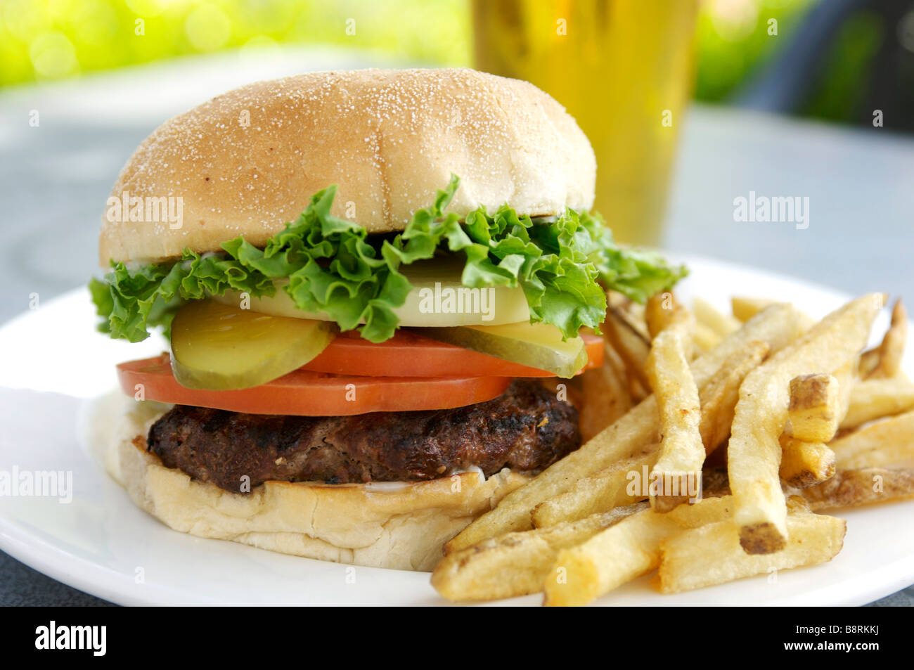 Hamburger with fries.  Loaded burger with lettuce, tomato, pickle, and a glass of beer. Stock Photo