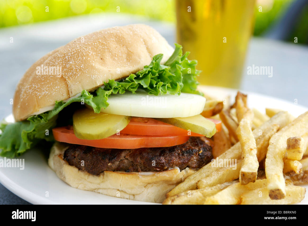 Hamburger with fries.  Loaded burger with lettuce, tomato, pickle, and a glass of beer. Stock Photo