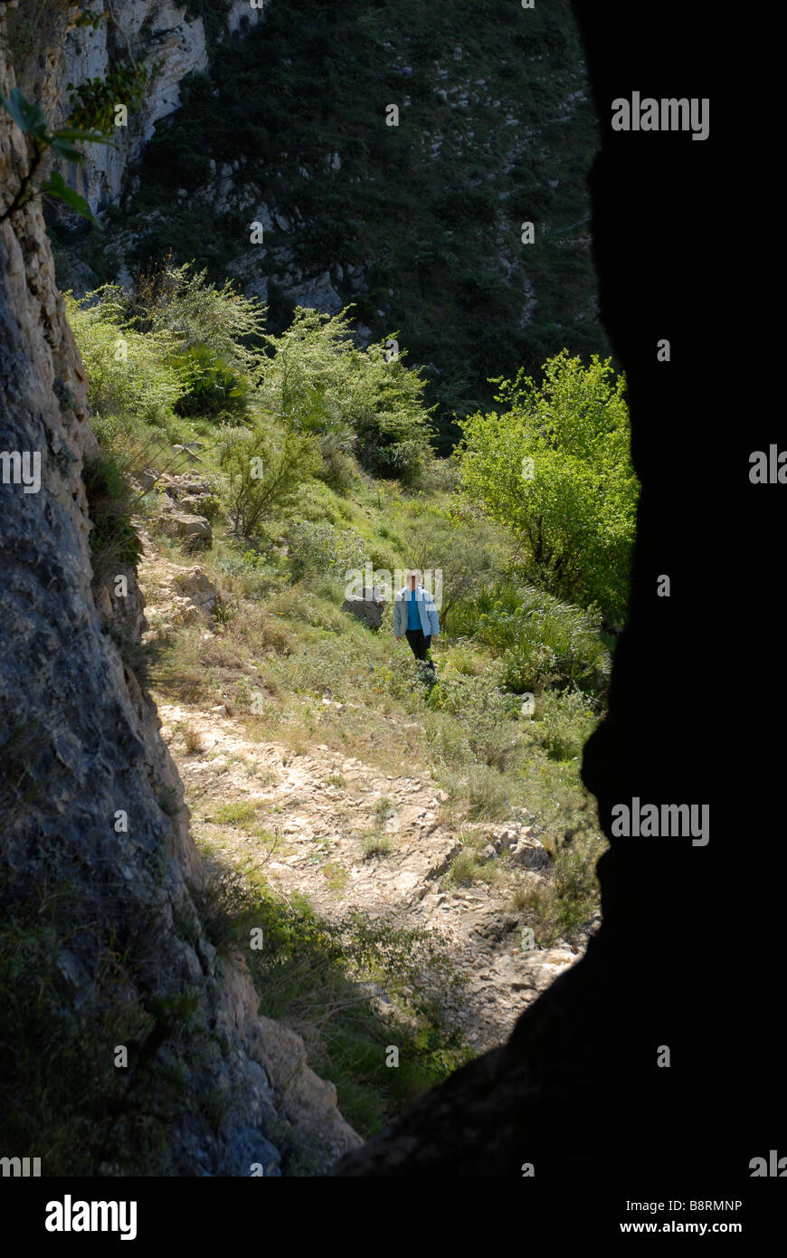 looking out of a cave to a woman walking past, Vall de Laguart, Benimaurell, Alicante Province, Comunidad Valenciana, Spain Stock Photo
