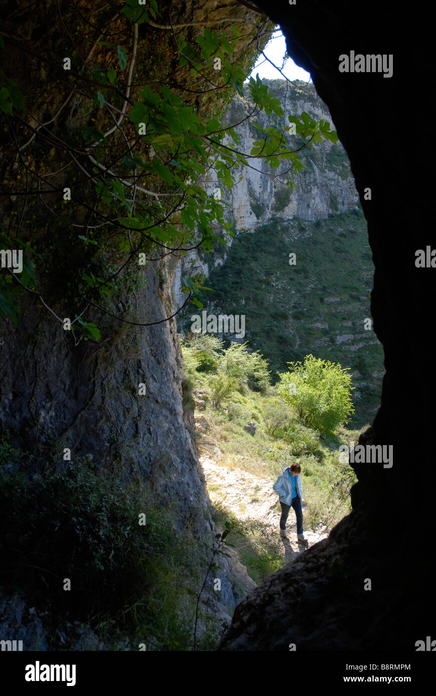 looking out of a cave to a woman walking past, Vall de Laguart, Benimaurell, Alicante Province, Comunidad Valenciana, Spain Stock Photo