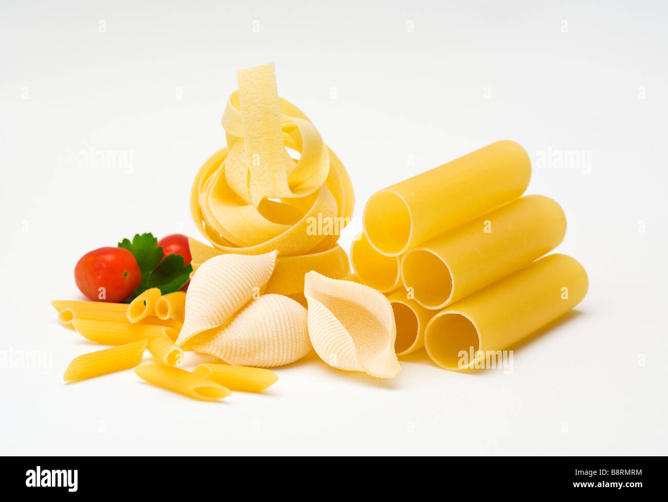 collection of raw pasta, tomato garnish, white textile surface Stock Photo