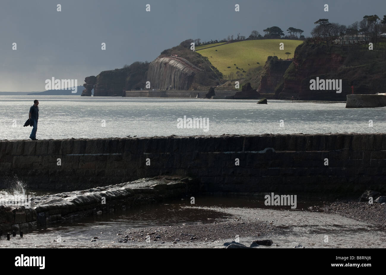 Lone figure walks along the sea wall Stock Photo - Alamy