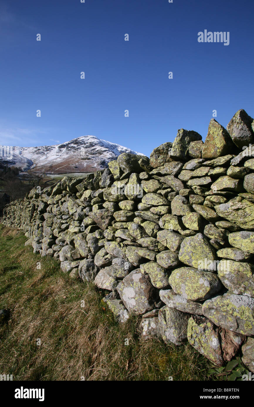 Dry stone wall leading to mountain peak on sunny day Stock Photo