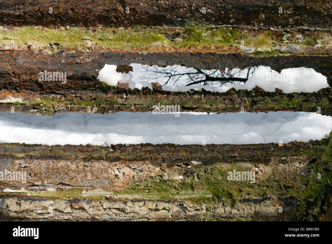 View through the hole in old metal bridge decking covered with snow on leafless tree branch. Stock Photo