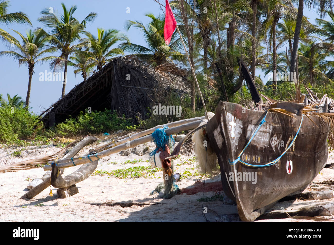 Indian national boat muchee walla on the Goa beach with hut in background with red flag, India Stock Photo