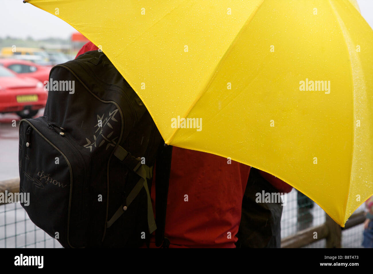 Spectator sheltering under yellow umbrella on rainy day at Thruxton Motor Racing circuit, Thruxton, Hampshire, UK Stock Photo