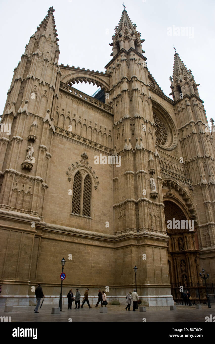 Worshippers and tourists walk beneath Mallorca Cathedral in Palma, Mallorca, Spain. Stock Photo