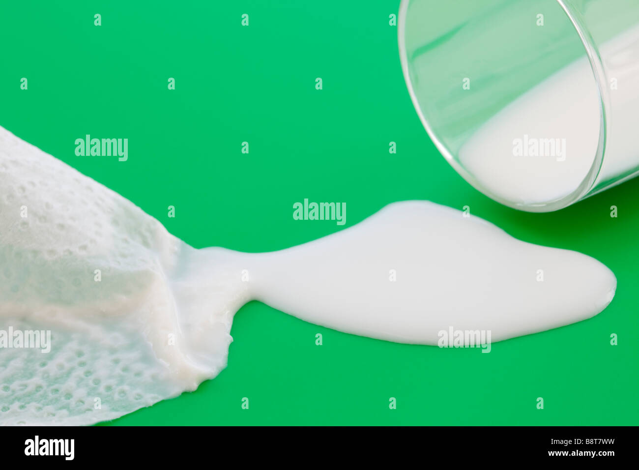 Paper towel cloth soaking up milk spilt from a glass onto a green