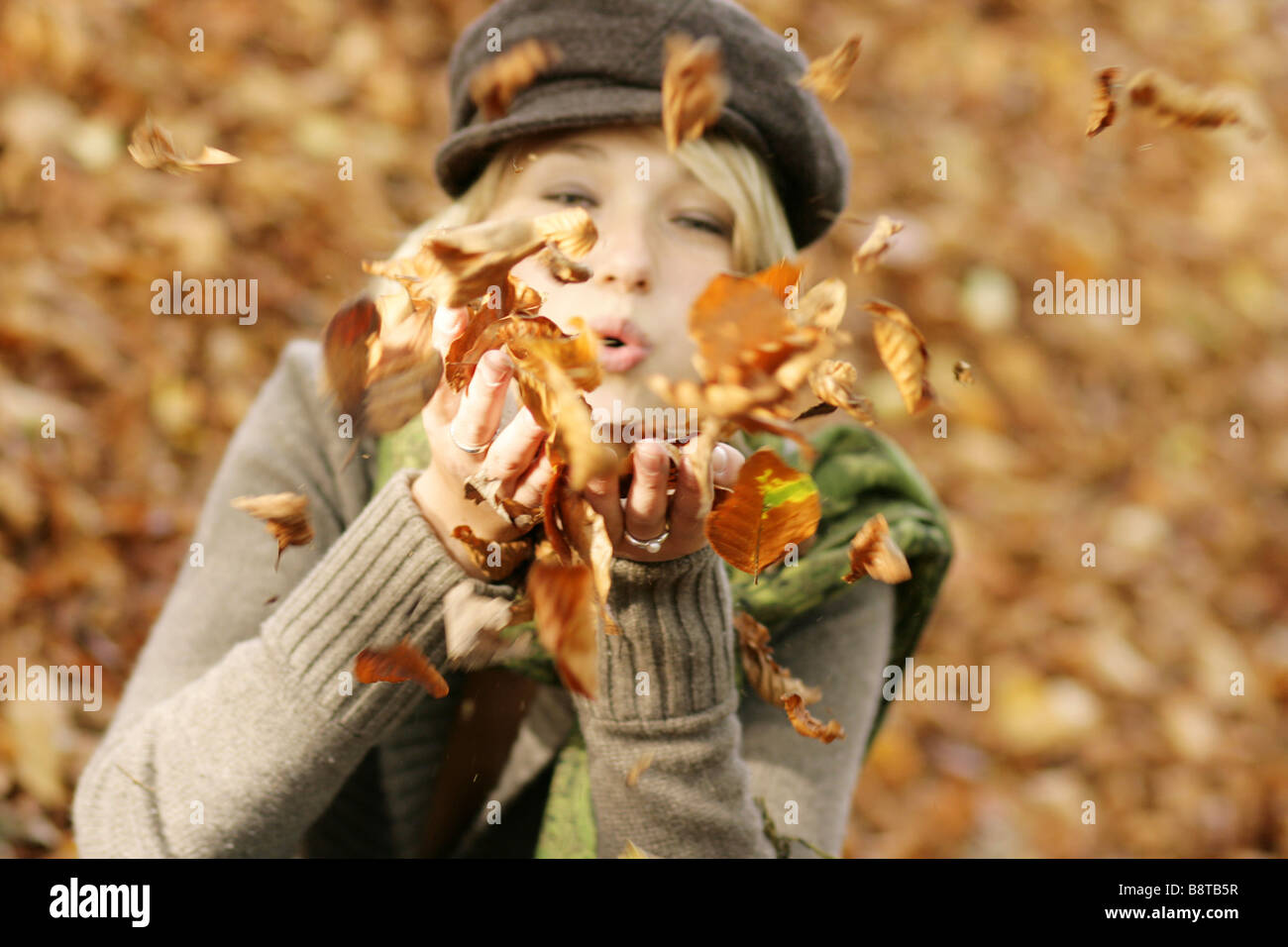 young blond girl with cap and scarf, playing with autumn foliage Stock Photo