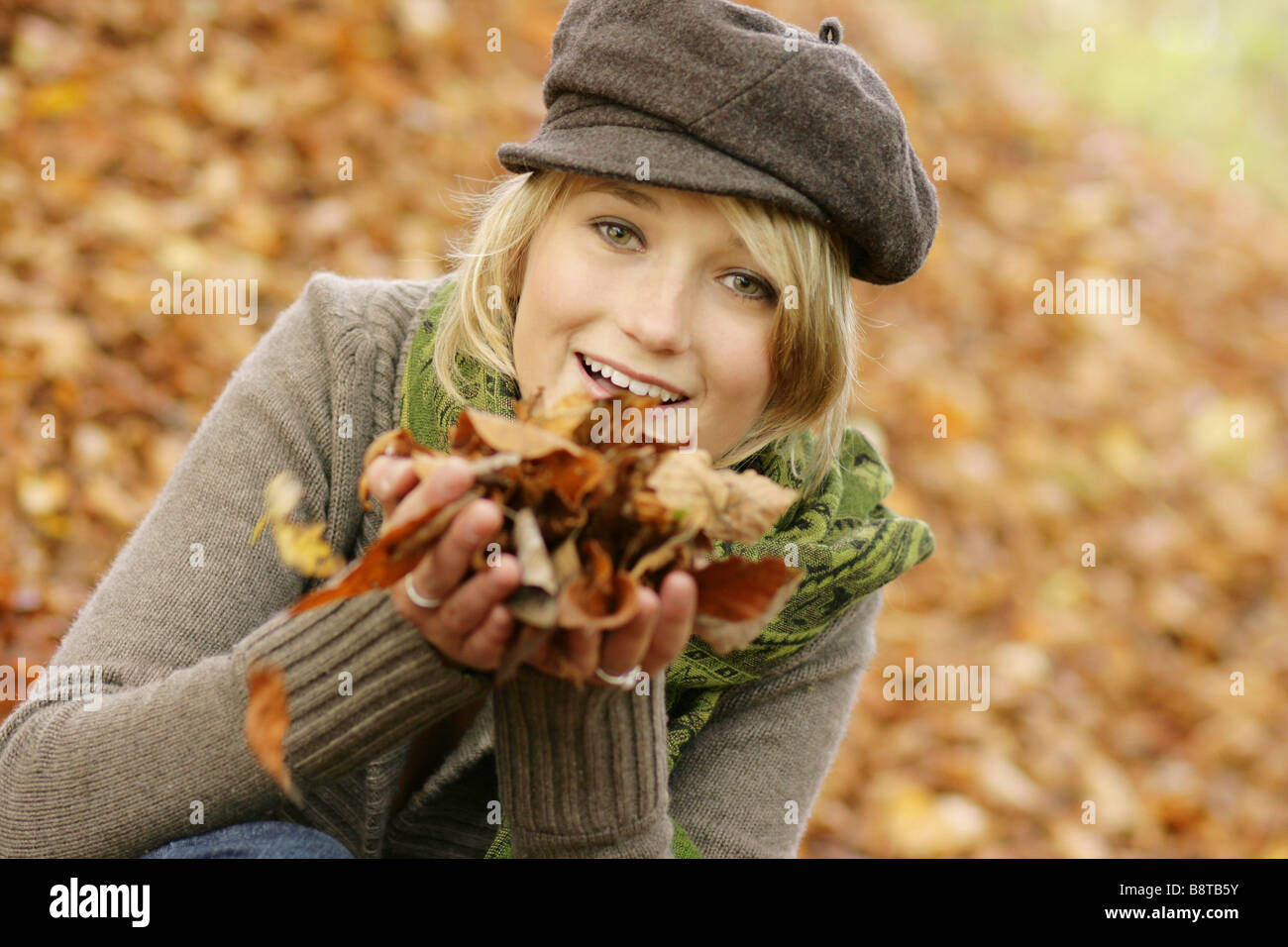 young blond girl with cap and scarf, playing with autumn foliage Stock Photo