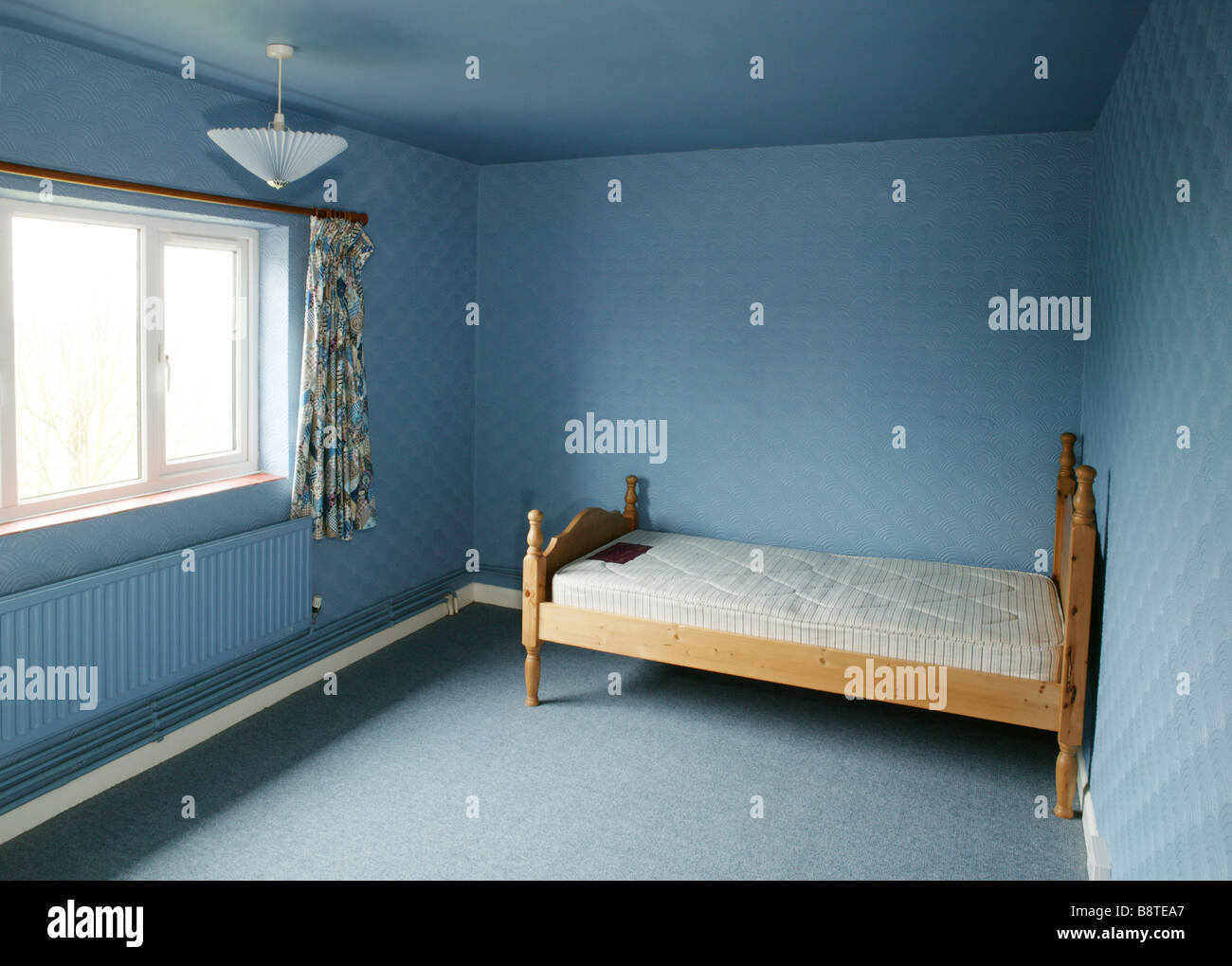 An empty blue bedroom with 1970 style artex walls and an empty bed in the corner Stock Photo