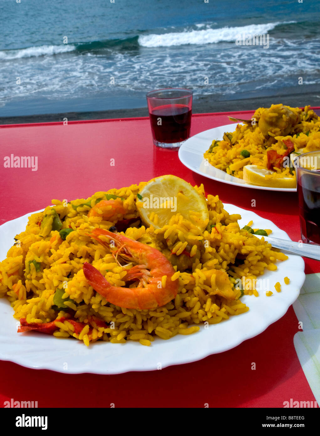 Spanish Paella Valenciana cooked and prepared by the sea, served with cool local red wine. Spain Stock Photo
