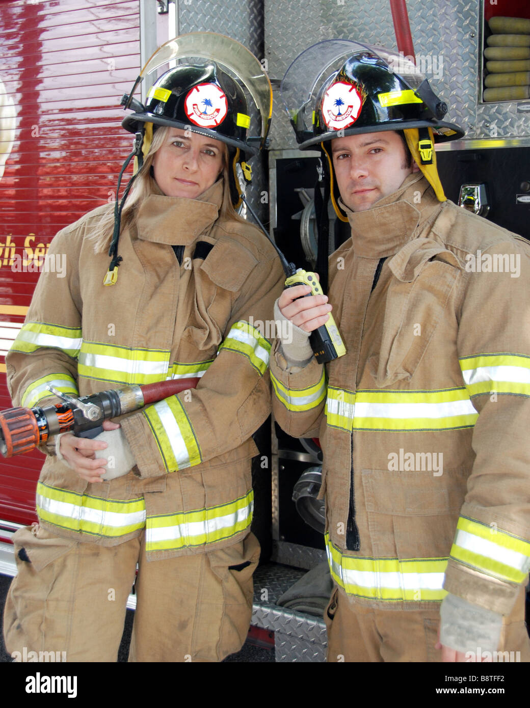 Male and Female Firefighters standing in front of fire truck with radio and hose Stock Photo