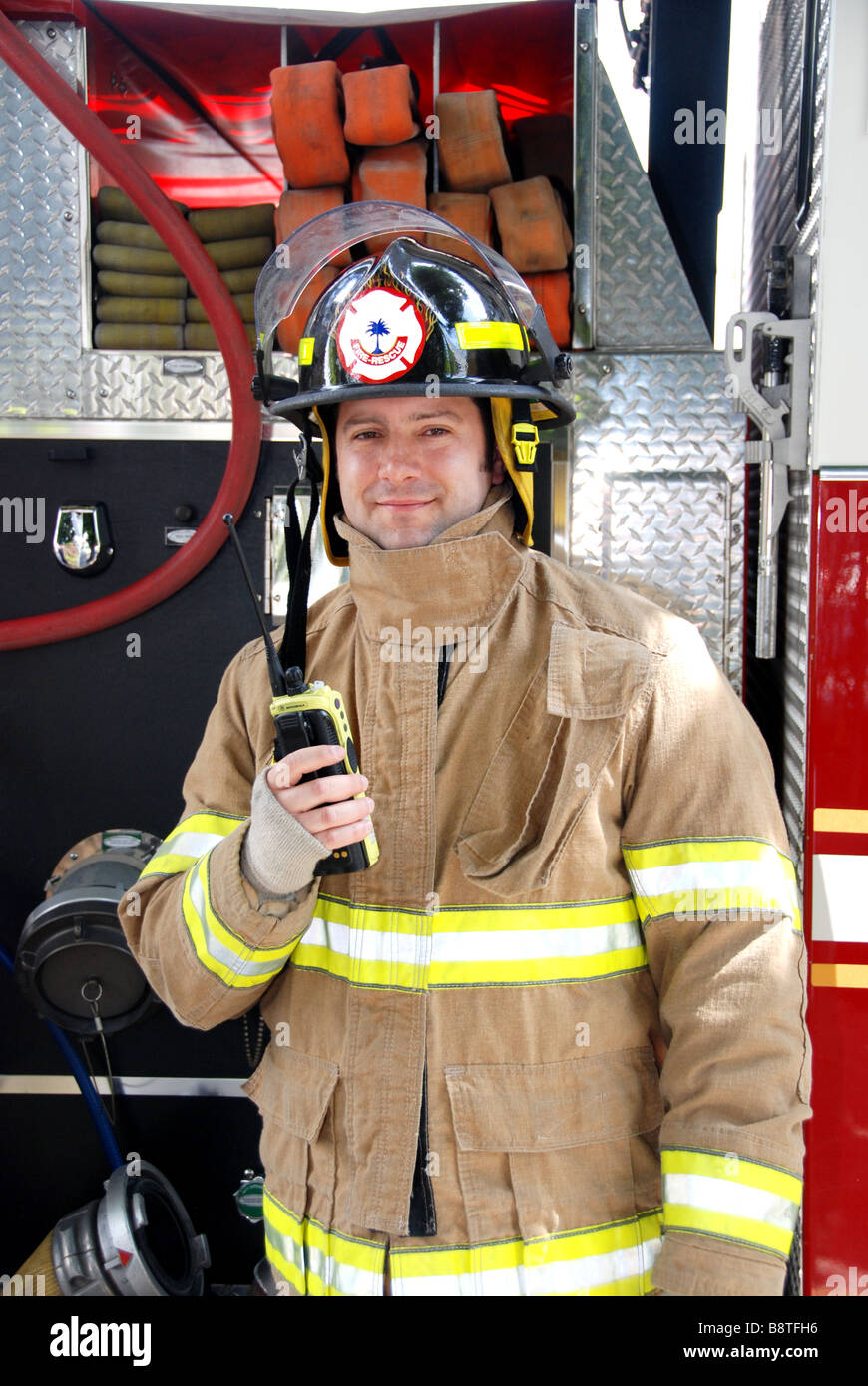 Smiling Male Firefighter holding radio in front of fire truck wearing bunker gear and helmet Stock Photo