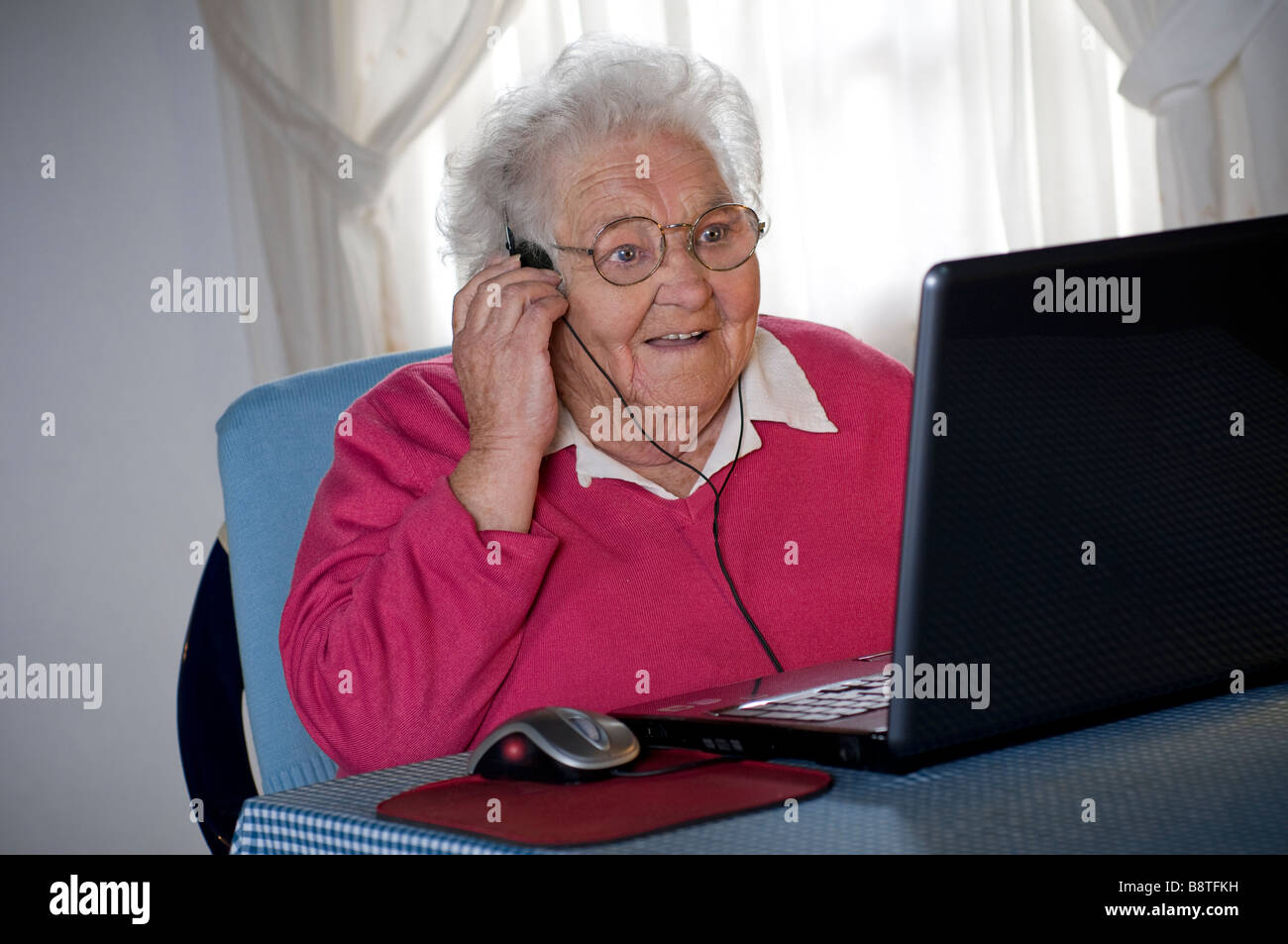 Senior elderly lady and laptop computer isolating covid-19 & headphones amazed by video chat zoom with family friends on her laptop computer screen Stock Photo