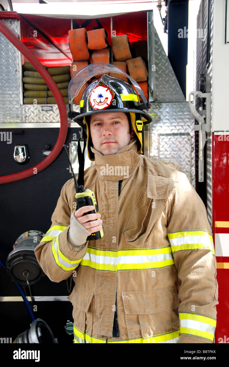 Male Firefighter holding radio in front of fire truck wearing bunker gear and helmet Stock Photo