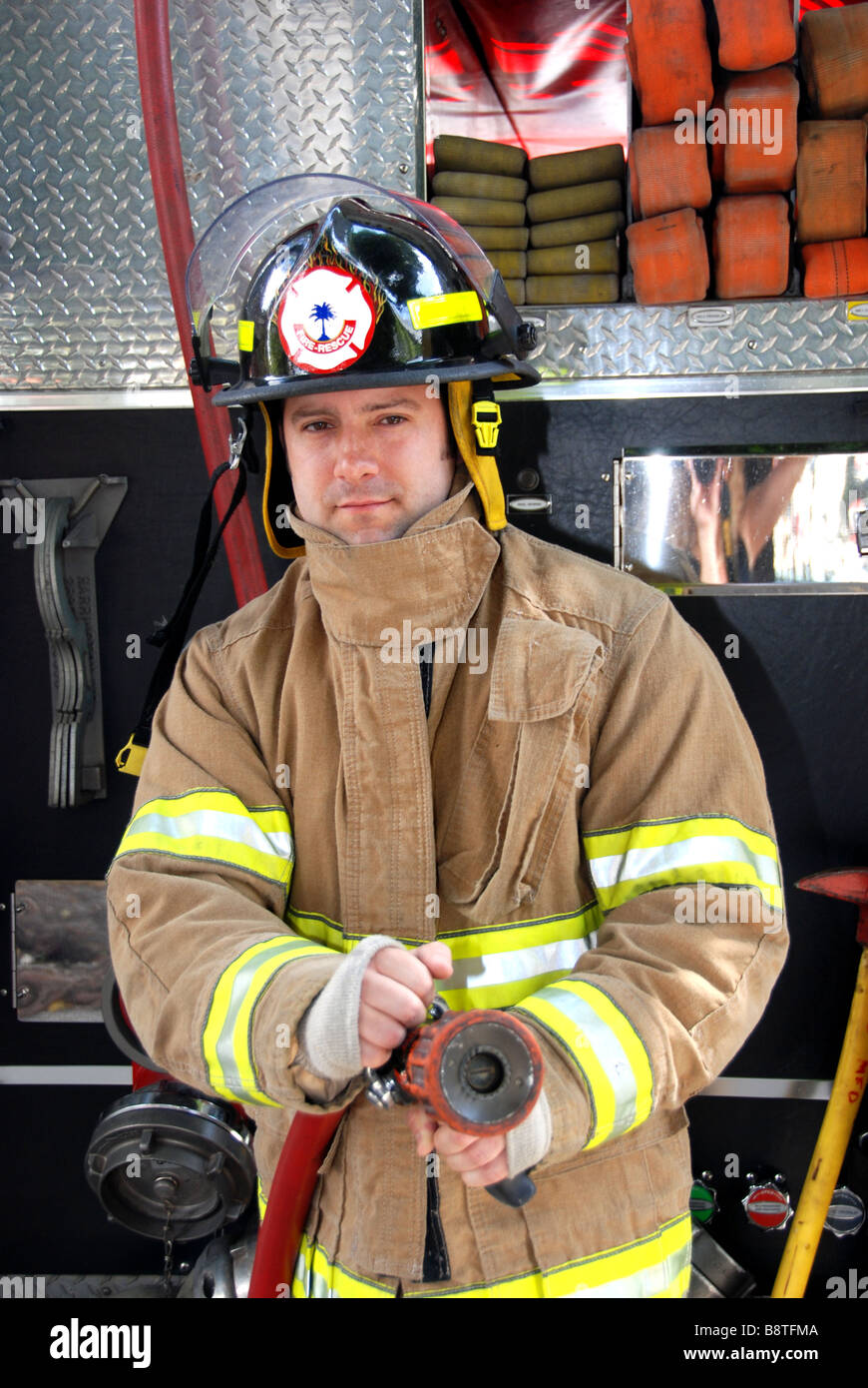 Male Firefighter holding fire hose in front of fire truck wearing bunker gear and helmet Stock Photo