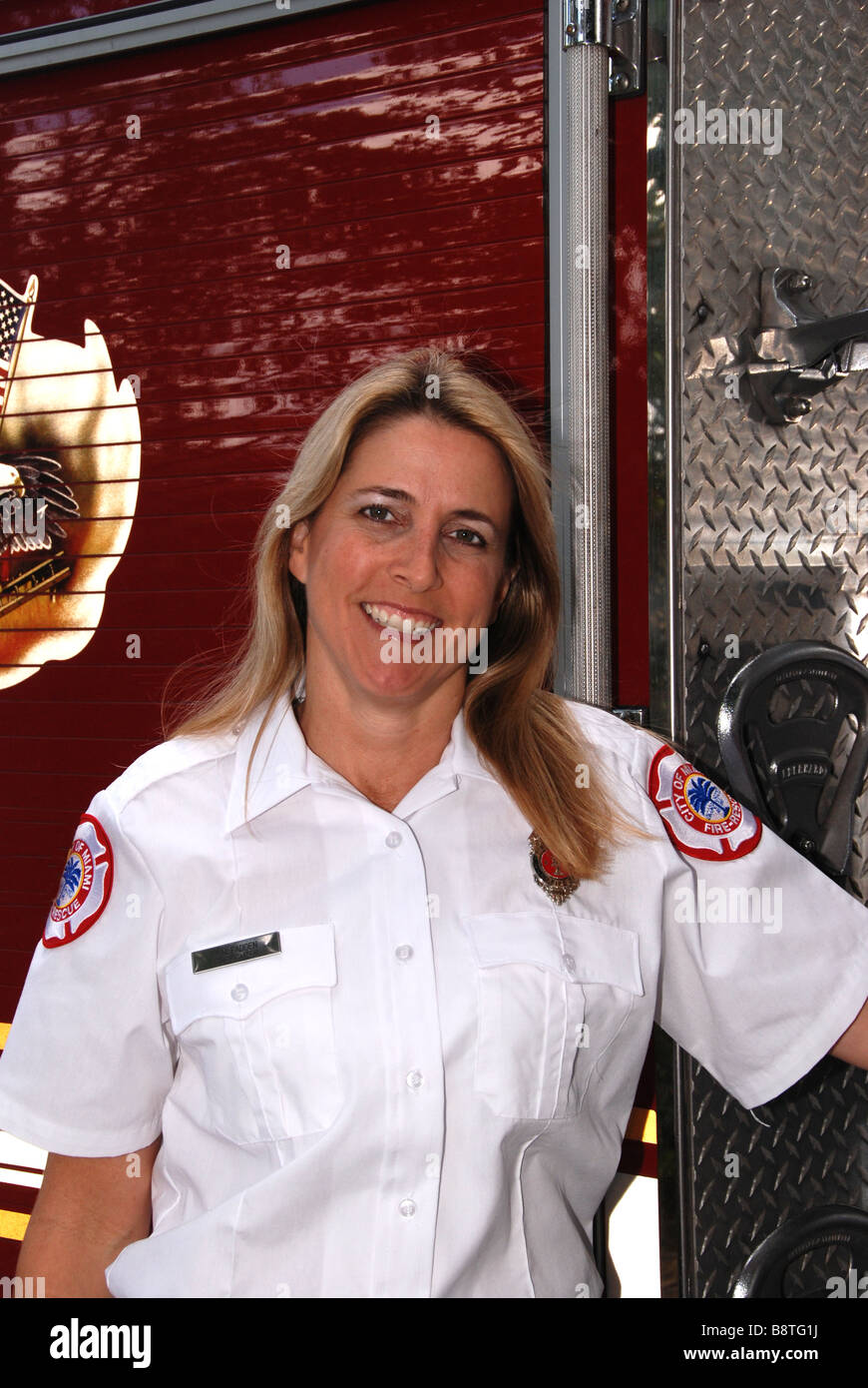 Smiling Female firefighter paramedic in dress uniform posing in front of fire engine Stock Photo