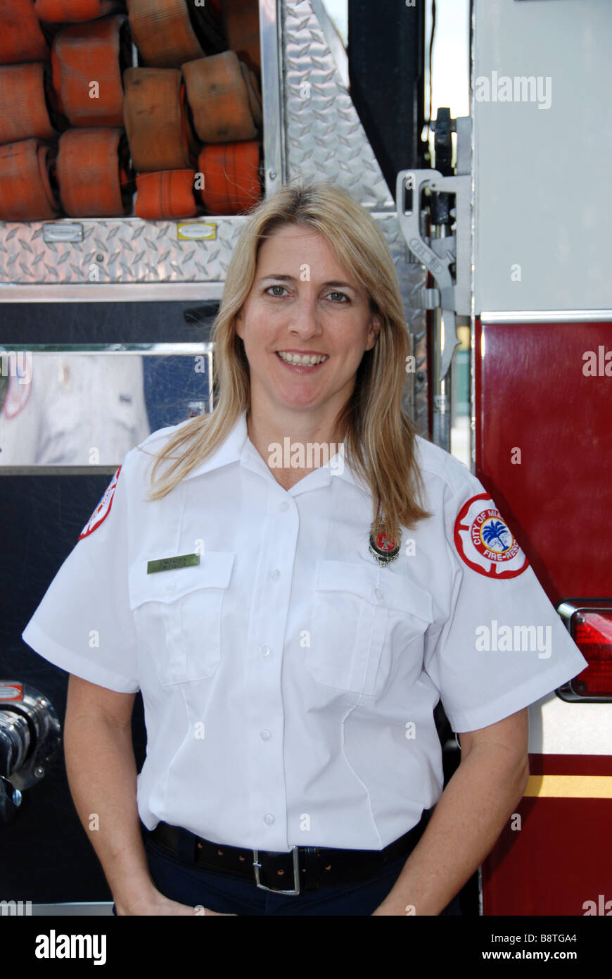 Smiling female firefighter paramedic in dress uniform posing in front of fire engine Stock Photo