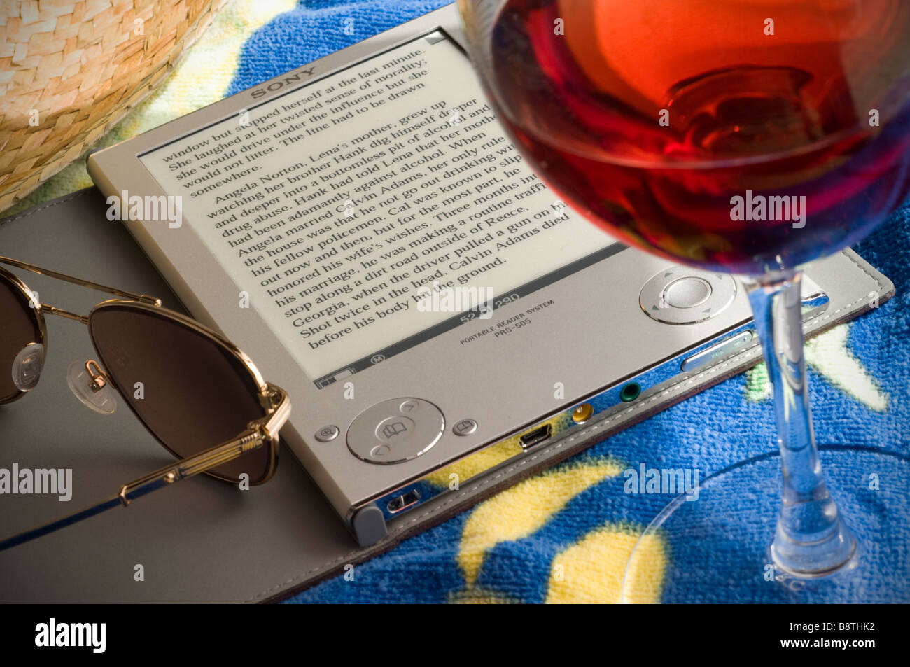 Sony eReader PRS-505, 2008 first generation electronic portable book reader reading device in vacation setting, with wine beach towel and sun glasses Stock Photo