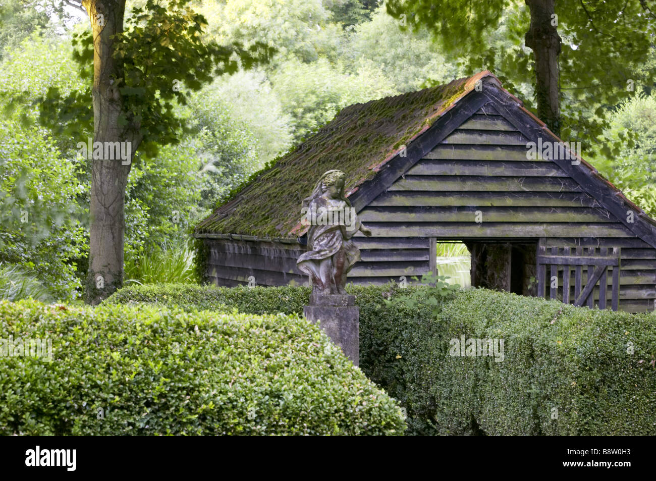 Statue and wooden boat shed below Harold Peto s water garden at Buscot Park Oxfordshire Stock Photo