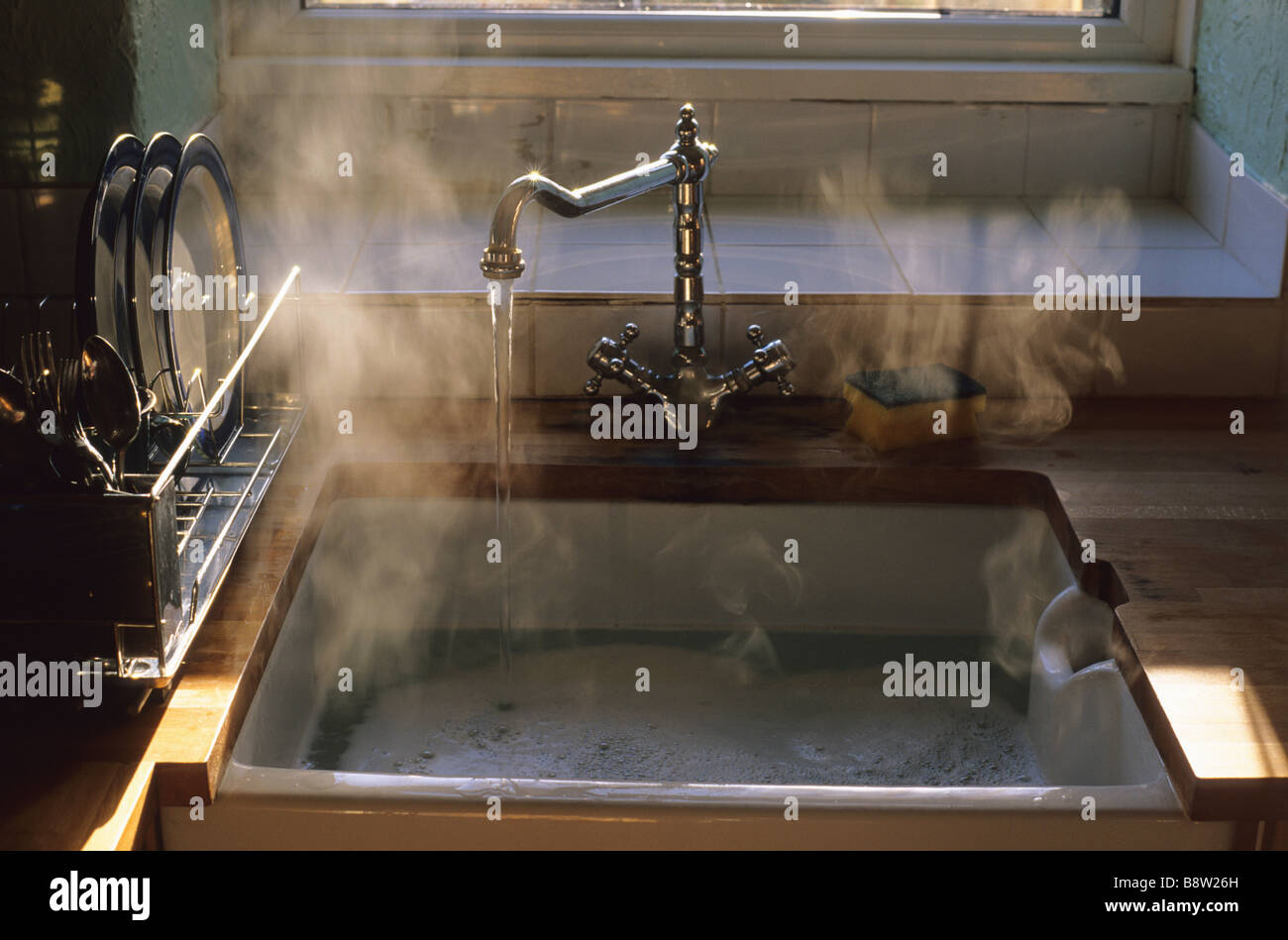 sunlight hitting steam rising from hot washing up water in kitchen sink Stock Photo