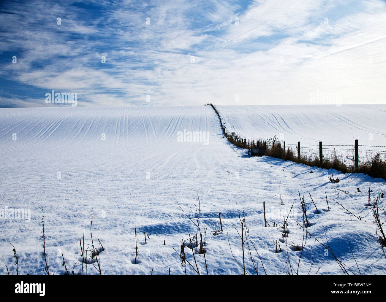 A sunny snowy winter landscape view or scene showing a snow covered field and cirrus cloud formation in a blue sky Stock Photo